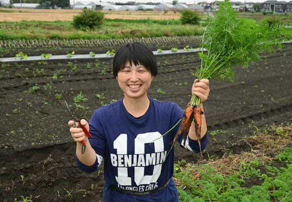 収穫した無農薬農業を手に笑顔を見せる早乙女さん