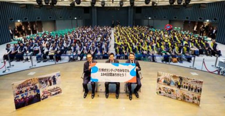 大阪・関西万博の運営を支えたボランティアスタッフと写真に納まる万博協会の石毛博行事務総長(壇上左)ら=15日午後、大阪市北区