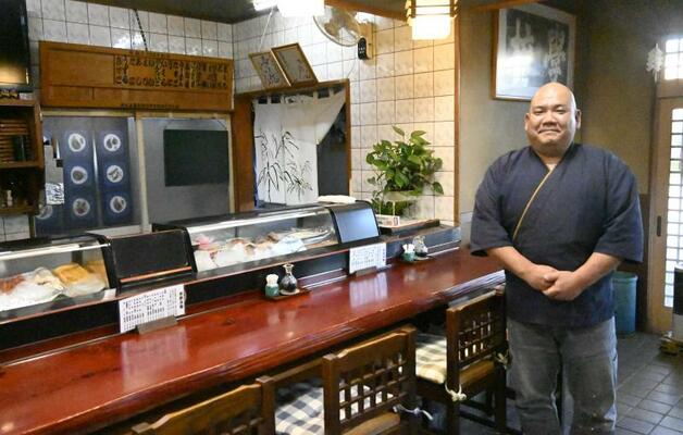 ネタが並ぶ陳列棚があるカウンター横に立つ戸塚さん