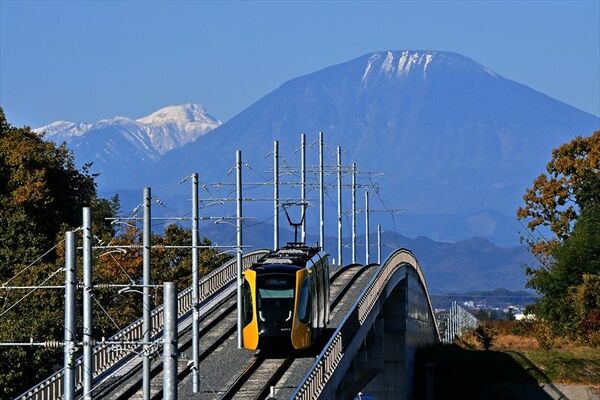 雪化粧した男体山（右）と日光白根山を望む山なりの軌道を走る列車＝21日午前10時20分、宇都宮市竹下町