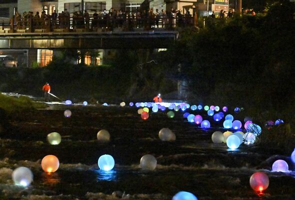 観光客らが見守る中、川面を流れる「やまほたる」＝25日午後８時40分、日光市湯西川
