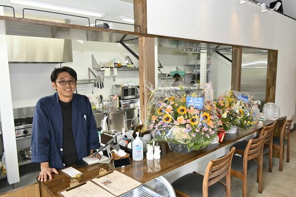 店主の長谷川さん。カウンターには開店の祝い花が並ぶ