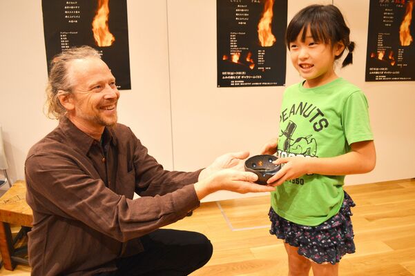 表彰式でブラックさんからお気に入りの器を受け取り笑顔を見せる栗田ことさん＝20日午後、ふみの森もてぎ