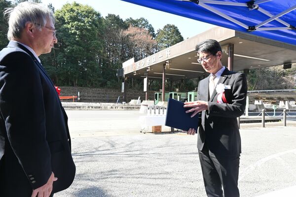 料金所前で引継書を読み上げる鈴木理事長（右）＝17日午前、鹿沼市深津