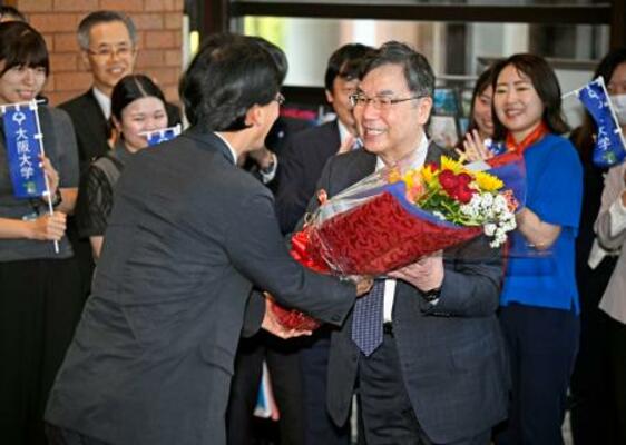 　ノーベル生理学・医学賞の受賞決定から一夜明け、大阪大の熊ノ郷淳学長（左）から花束を受け取る坂口志文特任教授＝７日朝、大阪府吹田市