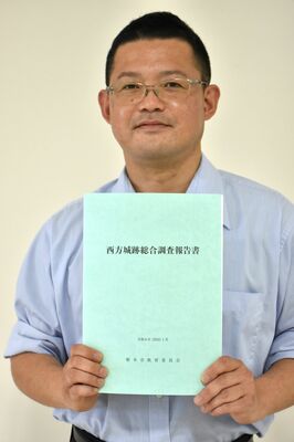 完成した西方城跡総合調査報告書を手にする市教委担当者の高見哲士主査