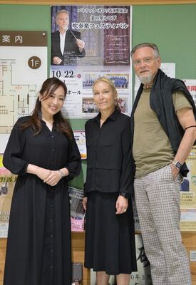 「美の里もてぎ　吹奏楽フェスティバル」のポスターを背にしたガロワさん（右）夫妻と栗田さん