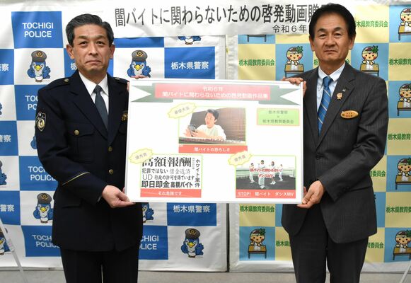 阿久澤教育長（右）にパネルを手渡す佐藤生活安全部長＝24日午後、県庁南別館