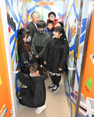 ラッピングされたエレベーターを見学する小菅町長（左奥）と睦小児童
