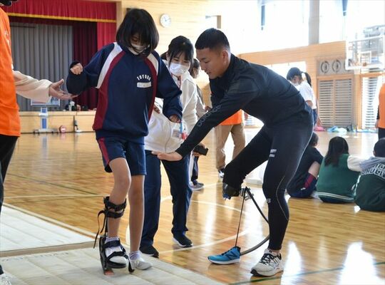 池田さん（右）の指導の下、義足歩行を体験する児童