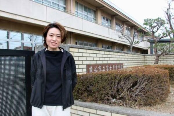 　通級指導教室の支援員として働いた母校の前に立つ新井麻衣良さん＝埼玉県熊谷市