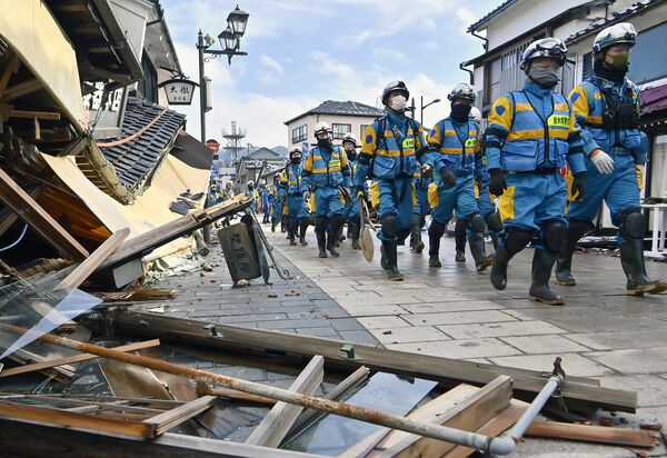 倒壊した建物の脇を通り、捜索活動に向かう県警の緊急災害警備隊＝14日午後１時30分、石川県輪島市