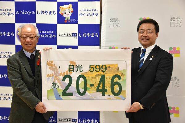 国交省に提案する日光ナンバーの図柄を手にする粉川市長（右）と見形町長＝2023年12月