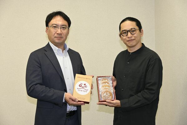 「豆乳キャラメル生サブレ」を持つ落合次長（左）と飯塚代表＝那珂川町