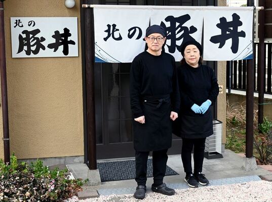 のれんの前に立つ大塚さん夫妻