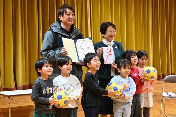 園児にボールを手渡し、大川市長（後列右）から感謝状を受け取った武井さん