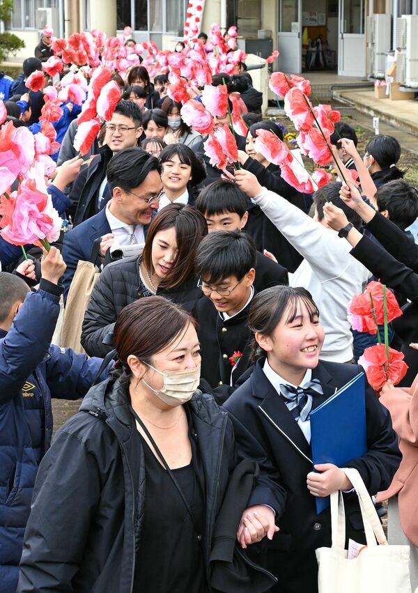 保護者と手をつなぎ、笑顔で花道を歩く卒業生＝19日午前11時45分、那須塩原市青木