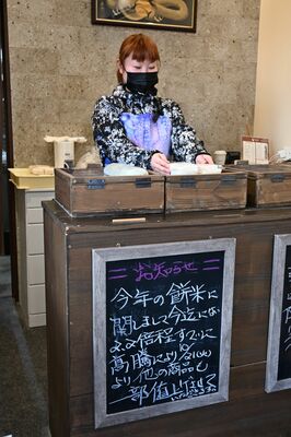 もち専門店で商品を並べる従業員。もち米の高騰や値上げについて掲示している＝27日午前、宇都宮市