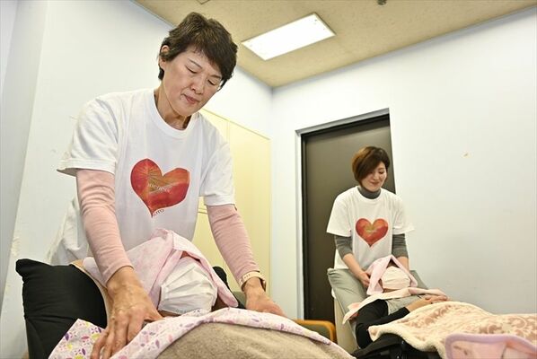 知人が作成した復興支援Ｔシャツを着て施術する加藤さん。右は娘の福田里江子さん＝31日午後３時、鹿沼市坂田山２丁目