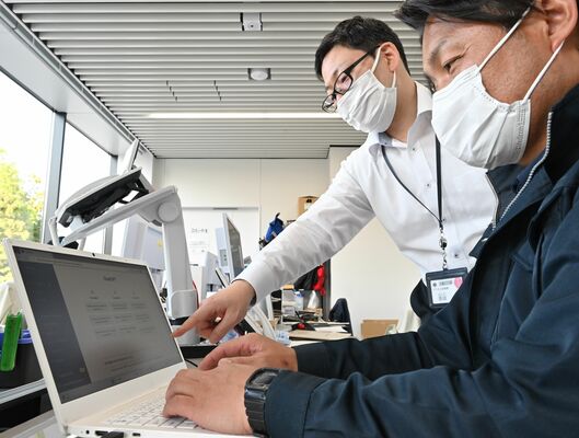 専用端末でチャットＧＰＴを体験する鹿沼市職員（右）＝９日午後、鹿沼市役所