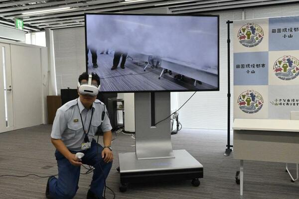 AR火災体験機器を実演する職員。職員の目に映る画面を映し出したモニターには、煙の映像が出現している。