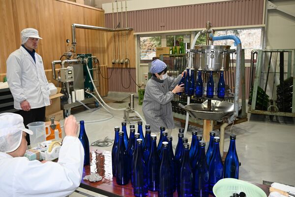 お酒の瓶詰め作業とお酒が詰められ、ふたが載せられた酒瓶＝２月１１日、鹿沼市上粕尾