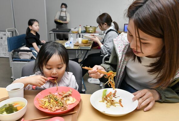 取材班が開設した子ども食堂「ほうぷけん」で焼きそばを頬張る親子＝10日午後６時55分、宇都宮市曲師町