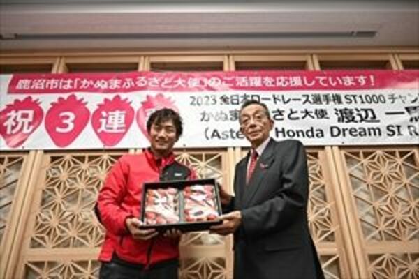 新しい横断幕の前で佐藤市長から記念のイチゴを受け取る渡辺選手（左）