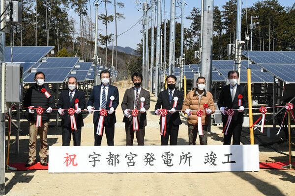 太陽光発電所の開所式でテープカットをする安田社長（中央）ら