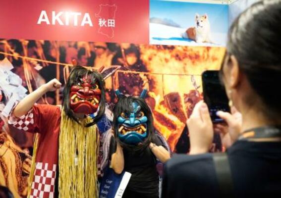 「トラストバンク」のブースでナマハゲに扮(ふん)して写真に納まる来場者=15日、香港(共同)