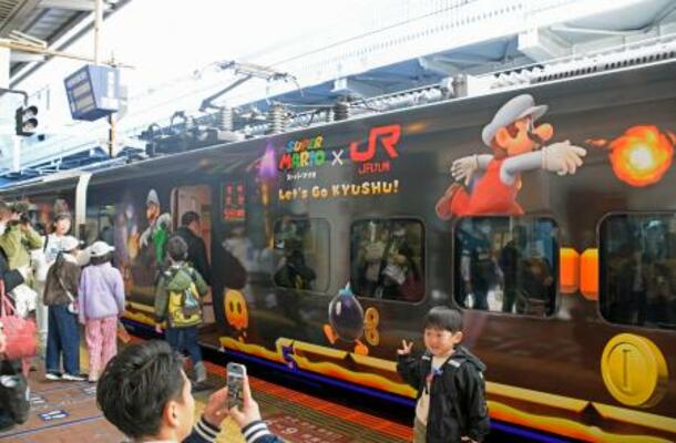 特別ラッピング列車「スーパーマリオトレイン」の前で記念撮影する人たち=29日午前、JR博多駅