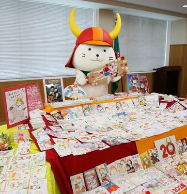 　届いた年賀状の山を前に羽子板を持って喜ぶ「ひこにゃん」＝７日午後、滋賀県彦根市役所