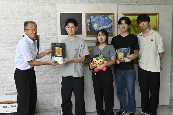 山下館長（左）から記念品のグッズを受け取る宇都宮大の学生グループ＝18日午前、宇都宮市桜４丁目