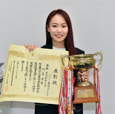 表彰状とトロフィーを手に笑顔の阿美さん