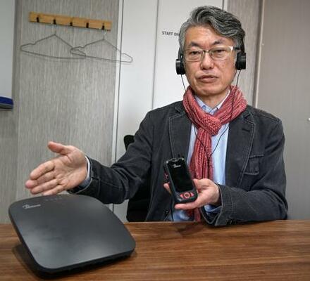 　「オーラキャスト」の機器を手にする東京工科大の吉岡英樹講師＝東京都港区