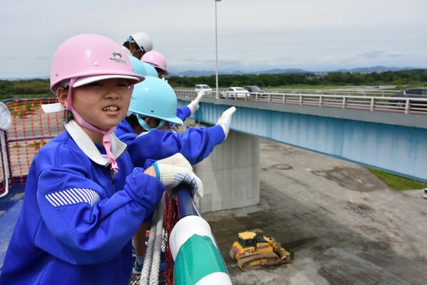 高所作業車に乗り板戸大橋建設工事現場を見学する児童たち