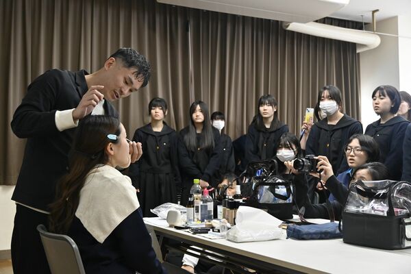 高校生の前でモデルにメークする山本さん（左）