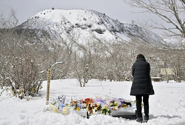 雪に覆われた事故現場を望む献花台の前で手を合わせる関係者＝27日午前11時45分、那須町湯本