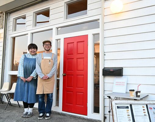 赤い扉が目印の店舗前に立つ生井さん夫妻