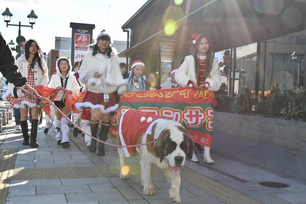 サンタクロースの仮装をしてパレードする犬と参加者