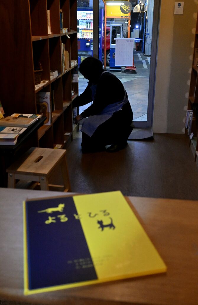 本棚を整理する大塚さん（奥）。絵本「よるとひる」を見て、かつての夜の孤独な時間を重ねた＝３月19日午後６時、宇都宮市曲師町、近藤文則撮影