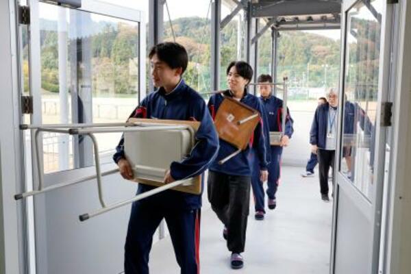 　石川県輪島市の県立門前高で、完成した仮設校舎に勉強机や椅子を運び込む生徒たち＝５日午前
