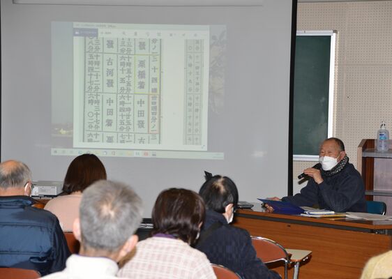 野木駅開業前の時刻表について説明する松本会長（右）
