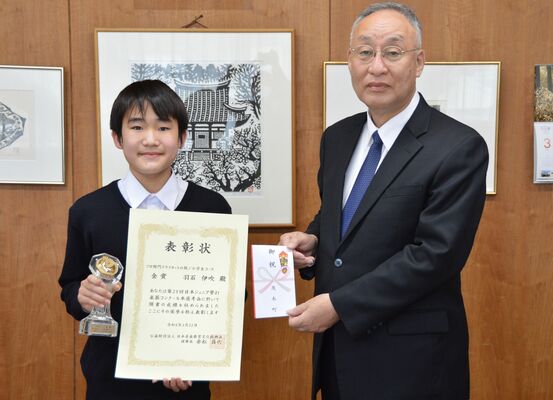 表彰状とトロフィーを手にした羽石さん（左）と、祝い金を手渡した古口町長