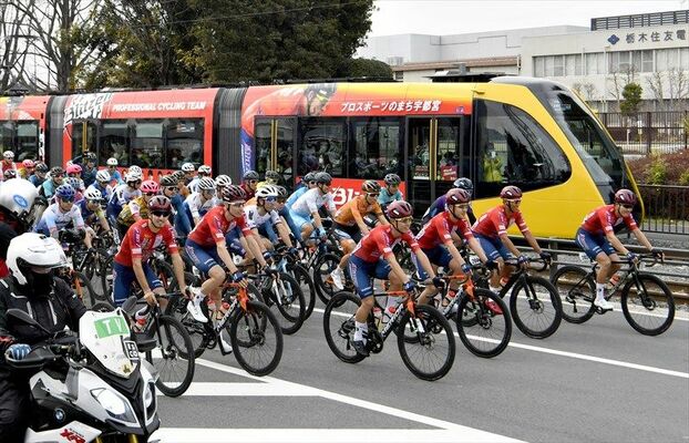 赤くラッピングされた列車と、先頭で並走する宇都宮ブリッツェンの選手＝24日午後２時、宇都宮市清原工業団地