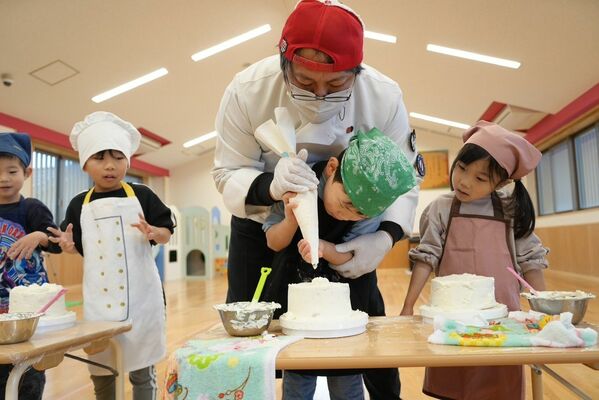 県幼稚園連合会の有志（中央）とケーキにクリームをのせる園児たち＝18日午前、石川県輪島市（同会提供）