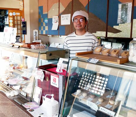 ショーケースにさまざまな菓子が並ぶ店内に立つ福島さん