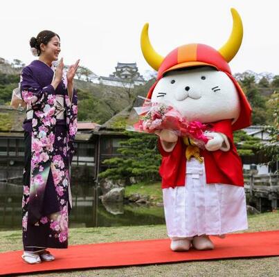 20回目の誕生日を祝う特別記念イベントで、大橋悠依さんから花束を受け取った「ひこにゃん」。奥は彦根城=13日午前、滋賀県彦根市