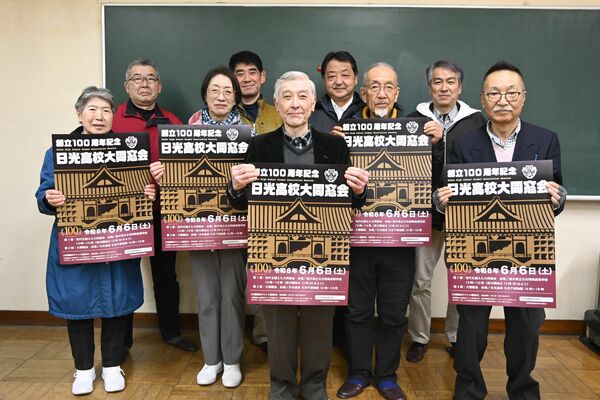 旧校舎をモチーフにした大同窓会のポスターを手にする実行委メンバーたち