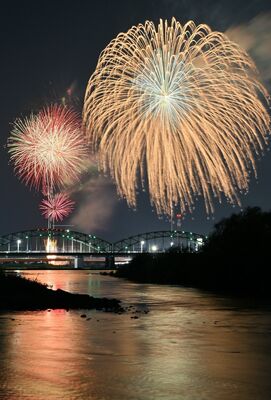 夜空や渡良瀬川の川面を彩る花火＝３日午後８時10分、足利市通４丁目（13秒間露光）